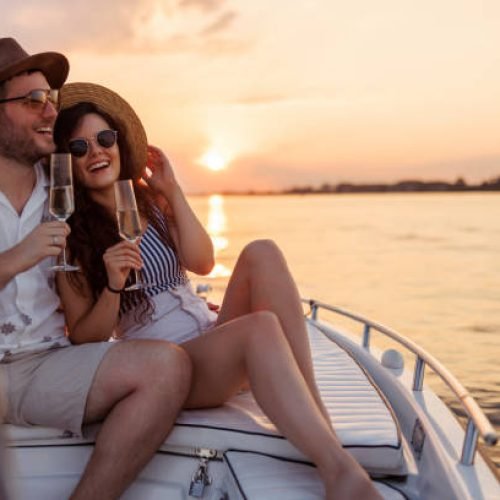 Couple in love enjoying summer vacation, hugging and drinking champagne while sailing to the sunset on a boat